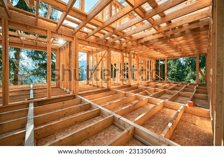Under-construction residential wooden frame home located near a forest. Commencement of a new construction project for a cozy house or a mountain cottage. Idea of contemporary ecological construction. Royalty-Free Stock Photo #2313506903