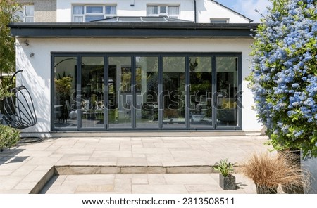 Stylish, closed, bifold doors with plants in spring, summer, revealing interior of a designer, lifestyle, kitchen diner room. Indian sandstone patio.