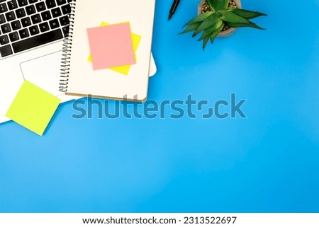 Laptop, notepad and paper reminders on blue background, flat lay.