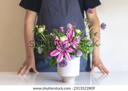 A man in an apron holds a vase of flowers, close-up.