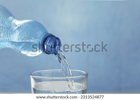 Fresh and cool water flows from the neck of the bottle. Water is poured from a plastic bottle into a glass. Copy space. Close-up