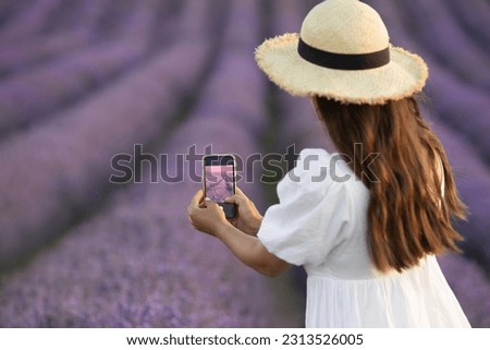 Close-up portrait from behind  asian woman takes a photo of lavander field on mobile phone. Tourism to provence lavender.