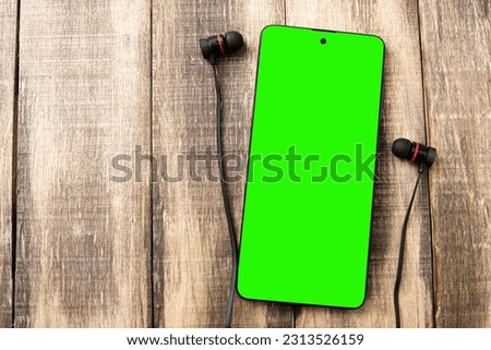 Mockup of a mobile phone with a chroma key screen. Smartphone with headphones on the table. Copy space