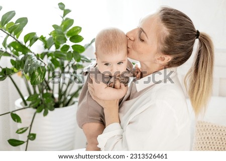 a young mother holds her little newborn baby in her arms in a bright bedroom, kisses him and admires him, mother's love and care for the child, mom and baby.