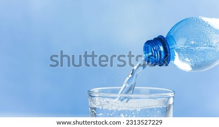 Horizontal banner with Fresh and cool water flowing from the bottle neck. Water is poured from a plastic bottle into a glass. Copy space. Close-up