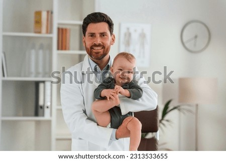 Holding boy in hands. Doctor with little baby is working in the cabinet.
