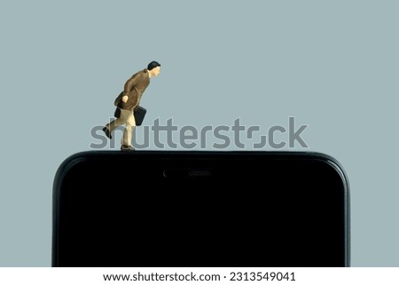 Miniature people toy figure photography. A businessman with briefcase running above blank black smartphone. Isolated on grey background. Image photo