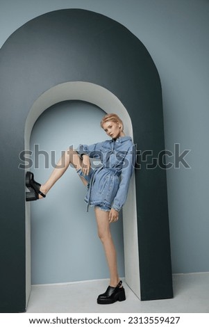 High fashion photo of a beautiful elegant young woman in pretty blue denim, jeans jumpsuit. Bicolor wall, light and dark blue. Blonde, slim figure, short haircut Royalty-Free Stock Photo #2313559427