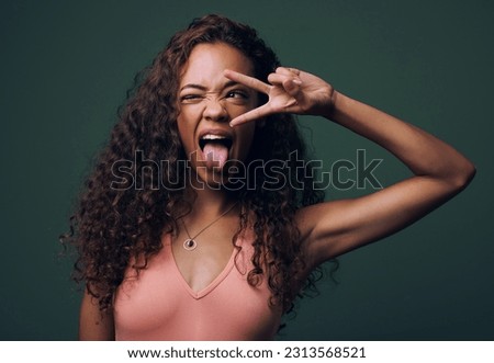 Tongue out, wink and peace by gen z girl in studio with hand, sign and gesture on green background. Face, fingers and female model with crazy, personality and youth aesthetic, emoji or isolated pose