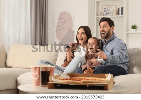 Excited family watching TV with popcorn and pizza on sofa at home, space for text