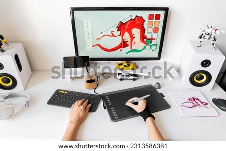 A young girl profession digital artist draws on a PC using a graphics tablet in her comfortable home office. Royalty-Free Stock Photo #2313586381