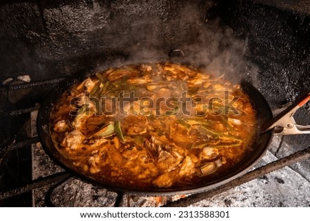 Traditional Valencian paella of chicken and rabbit cooked over firewood, rice, artichokes, garrfón, beans. Popular dish of Spanish cuisine. Royalty-Free Stock Photo #2313588301