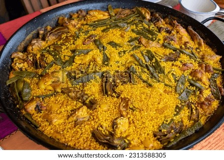 Traditional Valencian paella of chicken and rabbit cooked over firewood, rice, artichokes, garrfón, beans. Popular dish of Spanish cuisine. Royalty-Free Stock Photo #2313588305