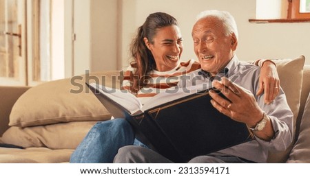 Portrait of a Nostalgic Woman Bringing the Family Photo Album to her Senior Father so They Can Watch Photos Together. Old Man Sharing Funny Memories and Stories with his Daughter