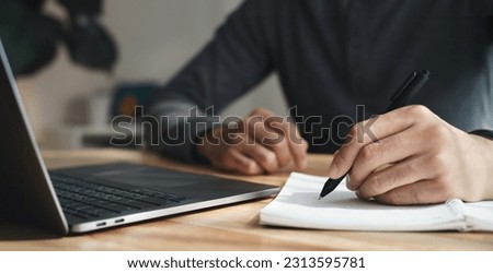 left handed man writes in a notebook on the table with laptop computer, Businessman. Royalty-Free Stock Photo #2313595781