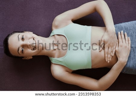 Top view of smiling young woman doing yoga and lying on floor with hands on stomach, copy space Royalty-Free Stock Photo #2313598353