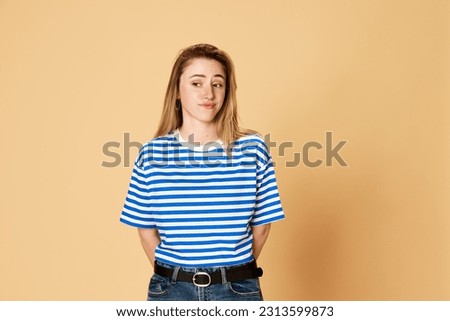 Portrait of young girl in striped shirt standing with doubtful face against yellow studio background. Misunderstanding. Concept of youth, human emotions, facial expression Royalty-Free Stock Photo #2313599873