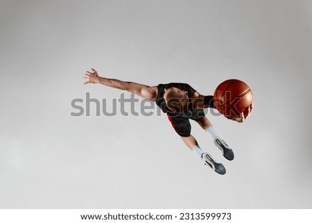 Motivated sportsman, male basketball player in motion, jumping with ball against grey studio background. Top view. Slam dunk. Concept of professional sport, healthy lifestyle, action and motion