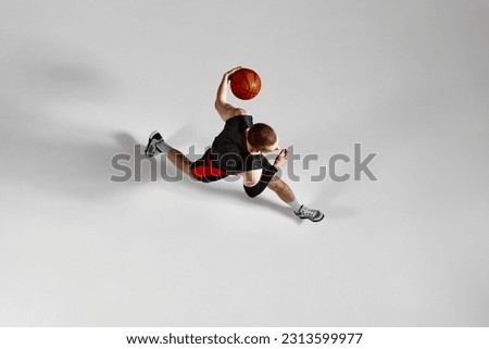 Young male athlete, concentrated basketball player in motion during game against grey studio background. Aerial view. Concept of professional sport, hobby, healthy lifestyle, action and motion Royalty-Free Stock Photo #2313599977