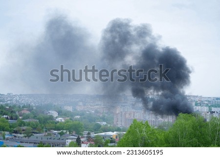 Black smoke rises over buildings and trees. Emergency concept. Royalty-Free Stock Photo #2313605195