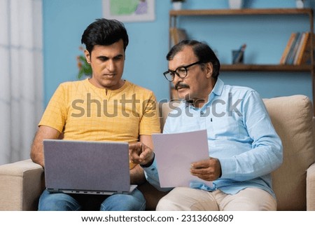 Indian elderly senior father with adult son discusing by checking some paper documents by using laptop - concept of information, fatherhood and investment planning Royalty-Free Stock Photo #2313606809
