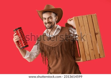 Handsome cowboy with explosive and wooden box on red background