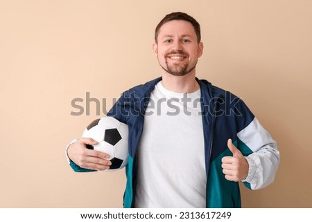 Happy man with soccer ball showing thumb-up on beige background