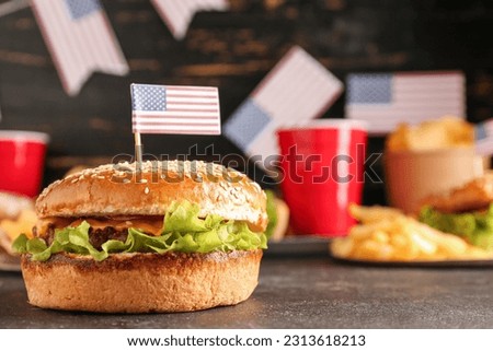 Tasty burger with paper American flag for Memorial Day celebration on dark table