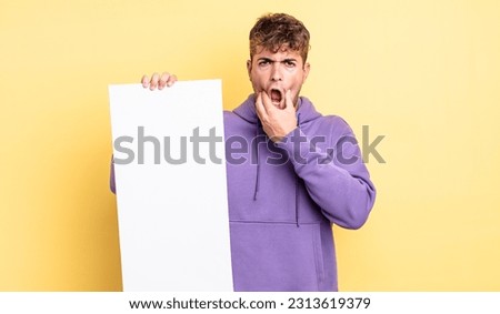 young handsome man with mouth and eyes wide open and hand on chin. copy space concept