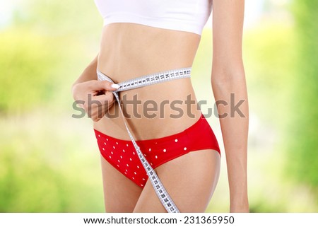 Young woman with measuring tape on bright background