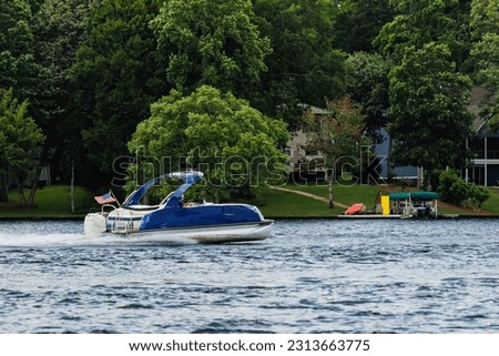 Boater on blue pontoon boat enjoying summer day on lake. Pontoon party boat cruising on freshwater lake. Royalty-Free Stock Photo #2313663775