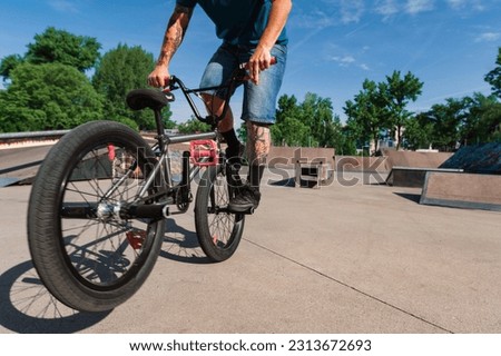 An unrecognizable tattooed guy is doing a 360 rotation trick on his bmx in a skate park. A cut-off picture of an urban tattooed professional bike rider doing a 360 rotation on his bike.