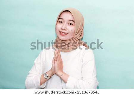 Portrait of a Asian Muslim Women wearing a hijab gesturing Eid Mubarak greeting on blue background