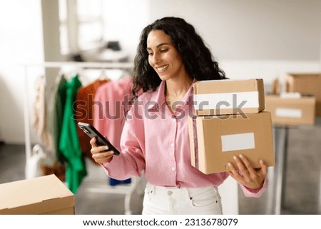 Clothing Shop Entrepreneurship. Happy Lady Using Smartphone Holding Packed Cardboard Boxes With Clothes And Outfits, Sending Message To Buyer Standing In Store. Small Retail Business, Ecommerce Royalty-Free Stock Photo #2313678079