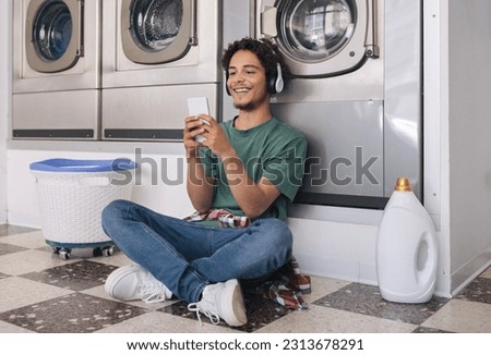 Easy Laundry. Happy Guy Using Smartphone Waiting While His Clothes Is Washing In Washer Machine, Enjoying Weekend Leisure And House Chores At Public Laundromat Service Indoor Royalty-Free Stock Photo #2313678291