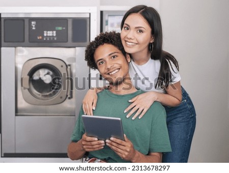 Laundry Service. Happy Young Diverse Couple Posing With Digital Tablet Hugging Near New Washing Machine Indoors, Booking Washer And Smiling To Camera Advertising Laundromat Service