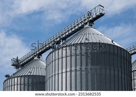 Steel grain storage silos with a conical bottom can be used for various purposes. Industrial facilities of feed and flour mills. Against the backdrop of a beautiful sky with clouds. Royalty-Free Stock Photo #2313682535