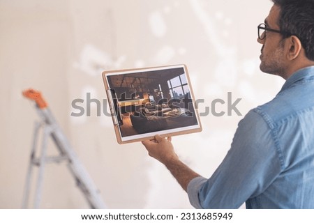 Young man in glasses doing renovation process in new apartment studies image focused home owner holding picture in hand contemplating modern loft-style interior design