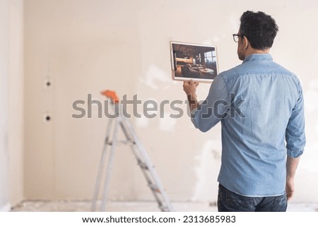 Man in glasses holding picture in hand looking at loft style interior design apartment owner standing against ladder near shabby wall in unfinished bedroom