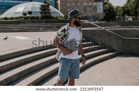 Photo of a freelance web designer young hipster guy with a modern netbook in the city. Carefree caucasian hipster spends his free time in the park.