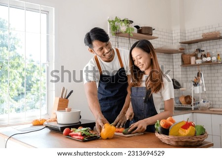 Asian couple happily prepare ingredient for breakfast in modern and stylish kitchen. Young Asian couple happily wearing apron and cooking together.
