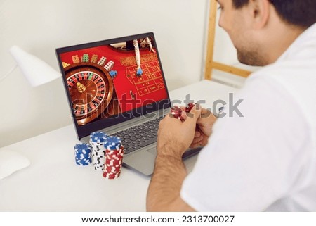 Gambling addict man plays and bets in online casino at home on his laptop computer. Online gambling concept. Man sits with poker chips and looks at laptop screen on which roulette game is played. Royalty-Free Stock Photo #2313700027