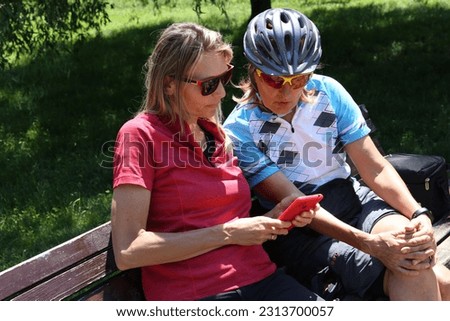 Two woman cyclist talking and laugh while relax and search route map on mobile phone. Summer healthy holiday.