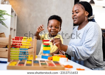 A cute little African child plays with colorful didactic educational toys. His proud mother supports him. Kindergarten teacher with child. Royalty-Free Stock Photo #2313711653