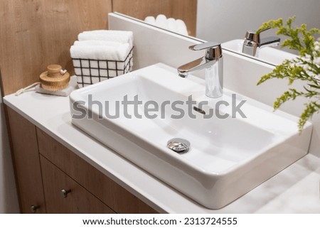 detail in interior of bathroom, modern ceramic wash basin with chrome water faucet, clean towels in metal basket and wooden massage brush Royalty-Free Stock Photo #2313724555