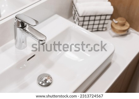 high angle view on shiny stainless steel water tap and white ceramic washbasin at bathroom with modern interior, selective focus on chrome faucet