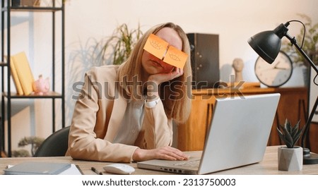 Inefficient tired businesswoman working sleeping on laptop computer with eyes stickers on face at office workplace desk. Young female lazy manager freelancer woman. Business people cheating to sleep Royalty-Free Stock Photo #2313750003