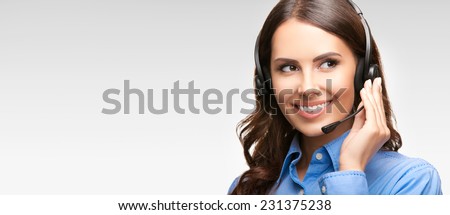 Portrait of smiling cheerful customer support phone operator in headset, with blank area for slogan, copyspace or product, against grey background Royalty-Free Stock Photo #231375238