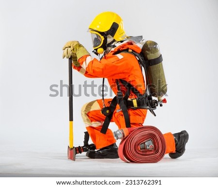 Firefighter knelt down and pressed his axe to the ground in a preparatory manner while having an oxygen tank on his back on a white background.