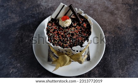 Cake. Simple Homemade Birthday Cake with colorful granules chocolate topping, slice of white and dark chocolate with fence decoration and gold ribbon. Served on white plate and soft blurry background